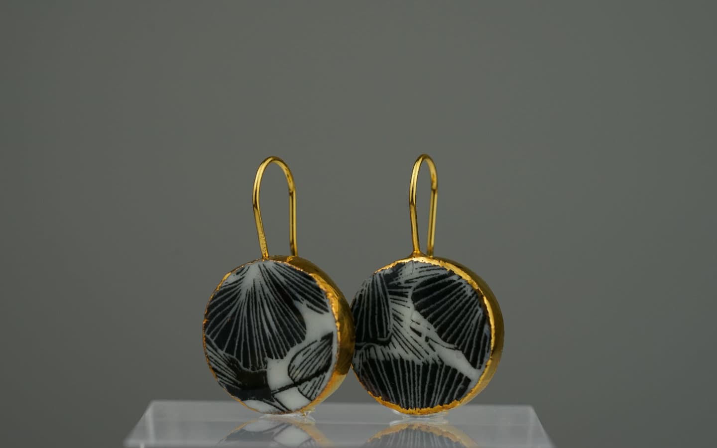 Diese handgefertigte Ohrringe aus Porzellan kombinieren das kontrastreiche Schwarz-Weiß eines Ginkgo-Motivs mit einem edlen Rahmen aus 24-karätigem Gold.